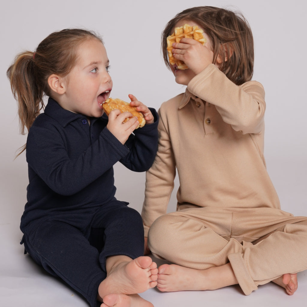 Two kids wearing The Leisure Set in beige and navy laughing and eating waffles