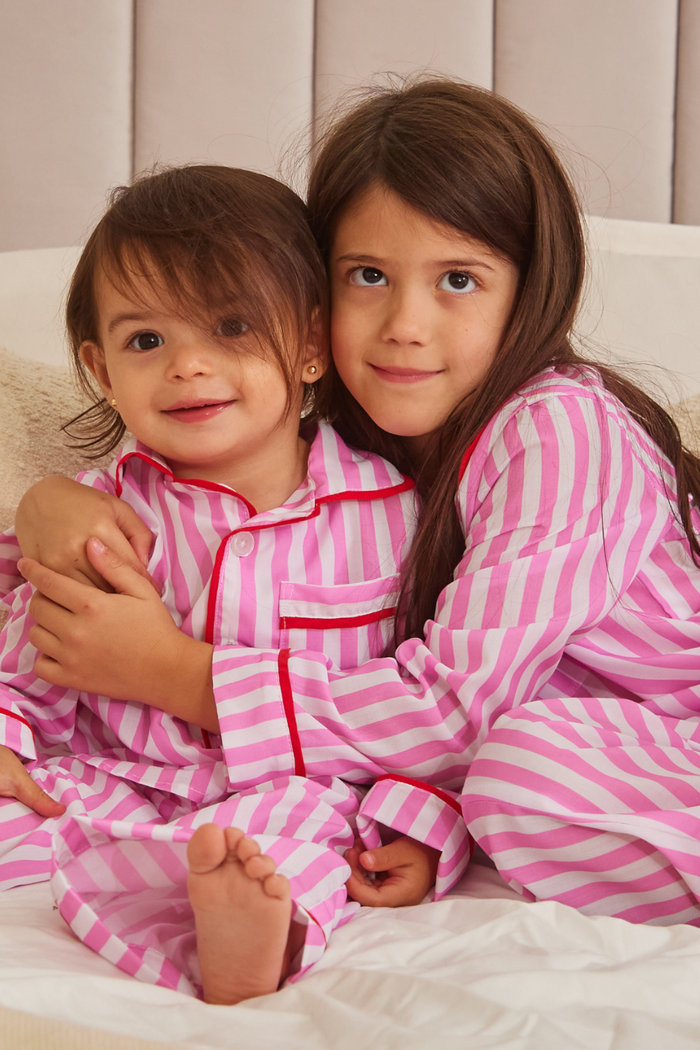 two girls sitting in matching stripe classic pyjamas with pink and white stripes and red piping