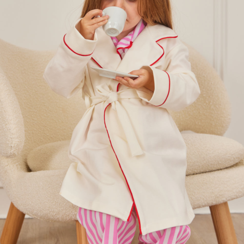 Kids cream piped robe by Midnight Palms, made from OEKO-TEX certified premium fabric, styled over pink stripe pajamas.